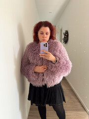 Woman in textured fur coat taking mirror selfie in hallway. Self-expression, fashion, and everyday...