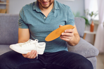 Man is sitting on the sofa, inserting an orthopedic insole into his shoe. Concept of orthopedic...