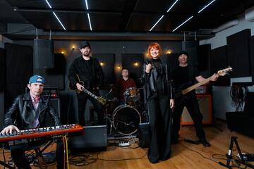 A music band rehearsing in a studio featuring a vocalist, guitarist, bassist, drummer, and keyboardist in a dynamic and creative atmosphere.