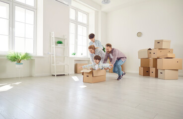 Happy parents in a new home play with children and cardboard boxes in the living room. Joyful...