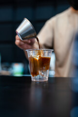 Closeup Barista hands pouring espresso shot to cup with cool water and ice making iced black coffee or iced Americano coffee