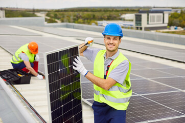 Smiling repairman with his colleague in high visibility clothing and hard hats are installing solar...