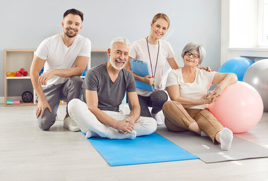 Happy portrait of a senior couple and trainers during a rehabilitation session or workout in the gym. The elderly patients receive guidance from the doctor and trainer while doing sport activities.