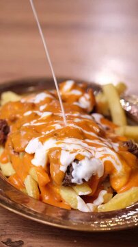 Stewed meat served on fried potatoes in Iskender kebab dish, topped with sauce. Close-up of Iskender kebab preparation.