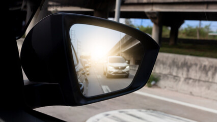 Mirror view of car. Cars coming from behind. And cars waiting in line. With dim light. There is a...