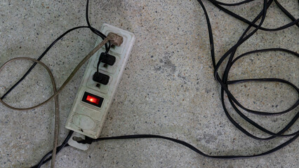 An old electrical outlet lying on the concrete floor. All three sockets are working. Wires are...