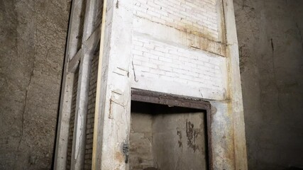 An old, abandoned elevator shaft with rusted metal and decayed concrete stands within a cave in Emen Canyon. The dimly lit structure suggests forgotten industrial use in a natural underground setting.