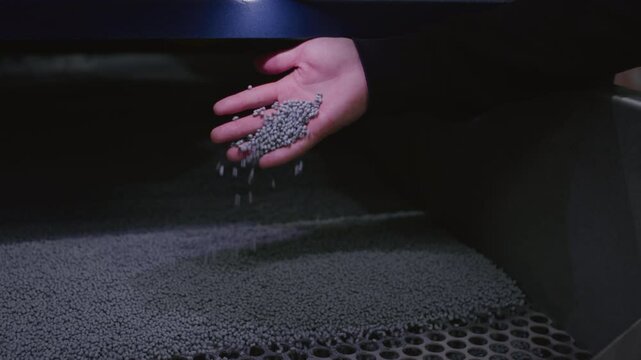 The hand touches the microplastic granules from the extruder. Plastic or polypropylene pellets on the conveyor belt of the machine. The engineer checks or inspects the raw materials for processing.