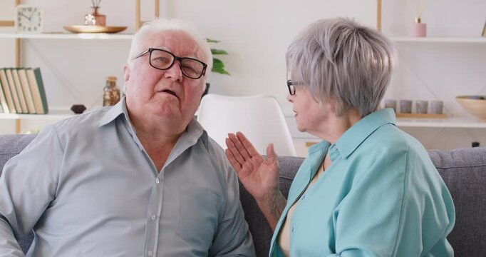 Senior couple talking at home. The deaf man, challenging to hear wife, leading to speak loudly. Impact of hearing loss on communication and the couple efforts to overcome this disability.