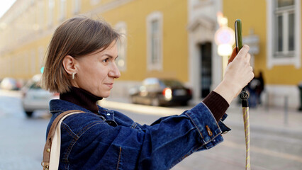A girl takes a photo on her phone while standing in the middle of a street in Lisbon and smiles