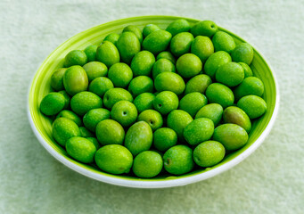 Beautiful kitchen plate with fresh green olives on monochrome green salad background. Olive dish...