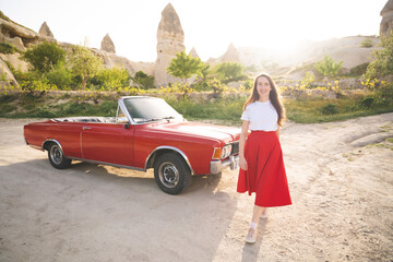 beautiful happy girl in a skirt posing near a retro car in the mountains of cappadocia