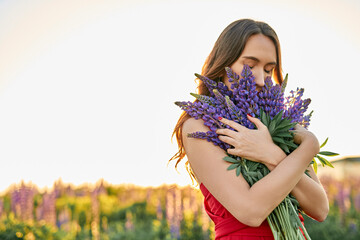 beautiful girl in a red dress with a bouquet of lupine flowers in the field