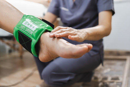 professional providing physical therapy assistance with weight cuff on patient ankle, focusing on rehabilitation and recovery