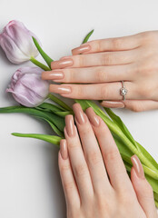 Woman showing nude manicure and purple tulips on white background