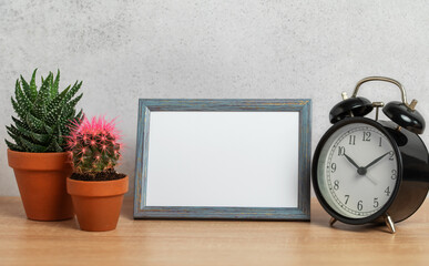 Empty frame, alarm clock and potted plants creating cozy home atmosphere