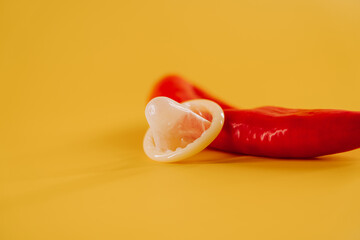 Red chili pepper and condom resting on yellow background for a bold visual statement