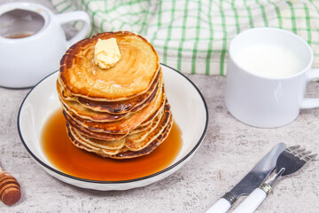 a dish of pancakes with honey,butter and cup of milk on the table as a breakfast menu
