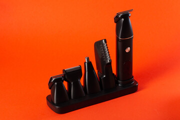 Modern set of hair trimmer with different attachments on a red background, close-up. Copy space for...