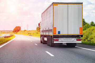 A modern truck with a semi-trailer transports consolidated cargo along a highway in the summer against the backdrop of the sun. Cargo insurance concept. 
