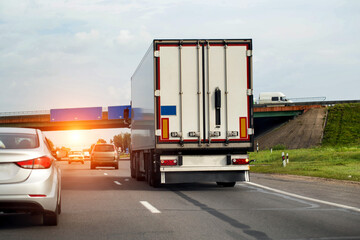 A truck with a semi-trailer is driving along the highway against the backdrop of sunset and car traffic. Concept of toll roads for trucks. Price per kilometer. Copy space for text, industry