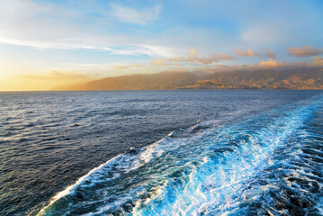 Sea view at sunset with distant shore and a ship trace