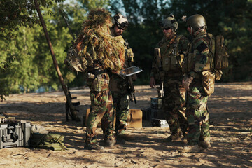 Troops assemble at the base, setting up a tactical plan, while the commander in grass camouflage...