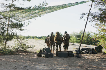 Soldiers leave the military base, heading into the field with long weapons on their shoulders,...