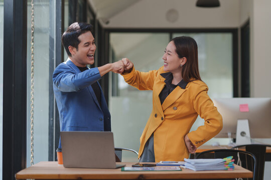 Two cheerful business professionals celebrating success in the office, sharing a fist bump that symbolizes teamwork and accomplishment, radiating happiness and motivation