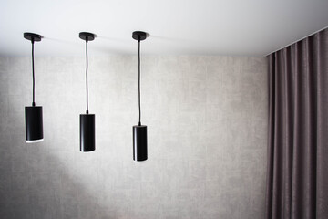 Modern black diode pendant lamps on a white stretch ceiling against a wall with a curtain. Copy...