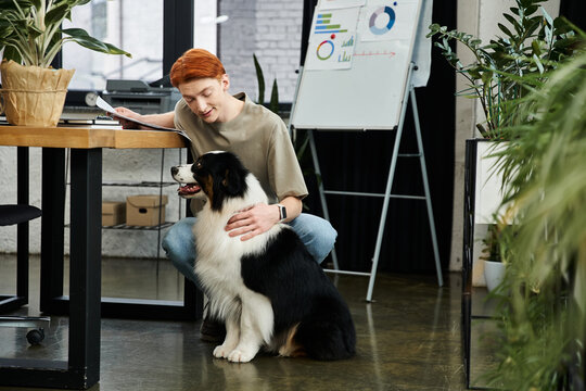 Young man with red hair shares a moment with a friendly dog in a modern office workspace