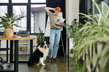 Young red haired man reviews documents while working with his dog in a modern office environment