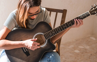 A talented young female musician sits alone and composes songs on the guitar. She plays a calm melody on a musical instrument.Music and hobbies.