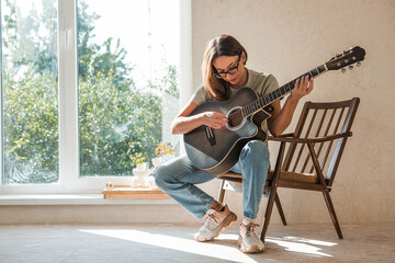 A talented young female musician sits alone and composes songs on the guitar. She plays a calm...