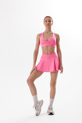 Young woman in pink athletic outfit poses confidently in a minimalist studio setting during a photoshoot