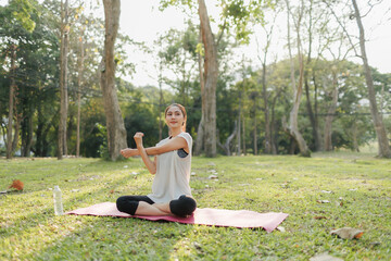 A young woman is practicing yoga in a public park, surrounded by a peaceful and shady atmosphere. She is wearing comfortable workout clothes and performing a yoga pose with focus and tranquility.