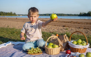 Fototapeta premium Young boy holds up a green apple during a picnic on a sandy beach