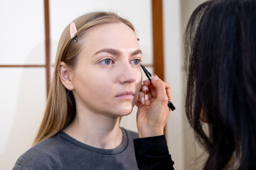 Professional makeup artist carefully applying eyeshadow to a young woman in a beauty salon. The...