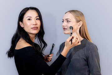 A professional makeup artist and a model pose together in a studio while holding beauty products....