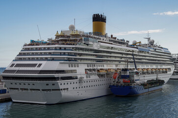 Modern cruiseship cruise ship liner Favolosa docked in Barcelona, Spain with bunker fuel vessel  and coast line beautiful landscape scenery and city skyline during Mediterranean cruising