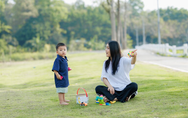 Fototapeta premium A mother and her child play joyfully in a public park, surrounded by laughter. The child runs around while the mother smiles and joins in, enjoying the warm sunlight and gentle breeze.