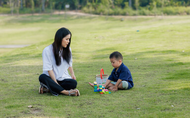A mother and her child play joyfully in a public park, surrounded by laughter. The child runs...