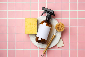 Spray bottle and eco friendly cleaning brush for washing dishes on plate on pink tile. Flat lay eco...
