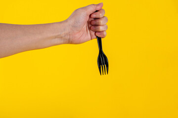 Hand and black fork on yellow background.