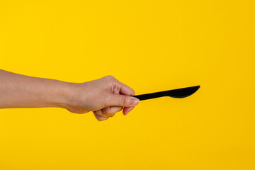 Black knife and hand isolated on yellow background. 