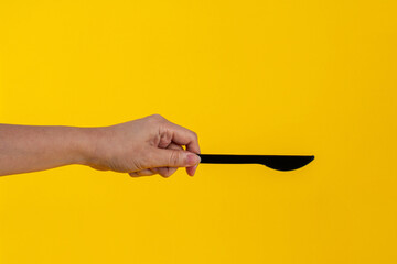 Black knife and hand isolated on yellow background. 