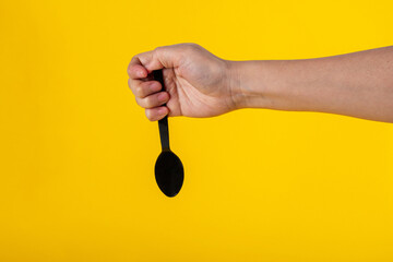 Hand and black spoon on yellow background.