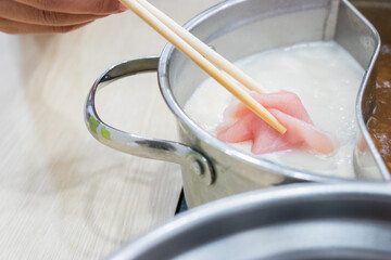 Shabu Shabu and Sukiyaki. Hand pick chopsticks sliced meat tong by chopsticks with hot pot background.