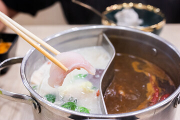 Shabu Shabu and Sukiyaki. Hand pick chopsticks sliced meat tong by chopsticks with hot pot background.
