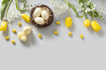 Easter frame with pastel chocolate eggs, tulip flowers, gypsophila and chick on light gray...